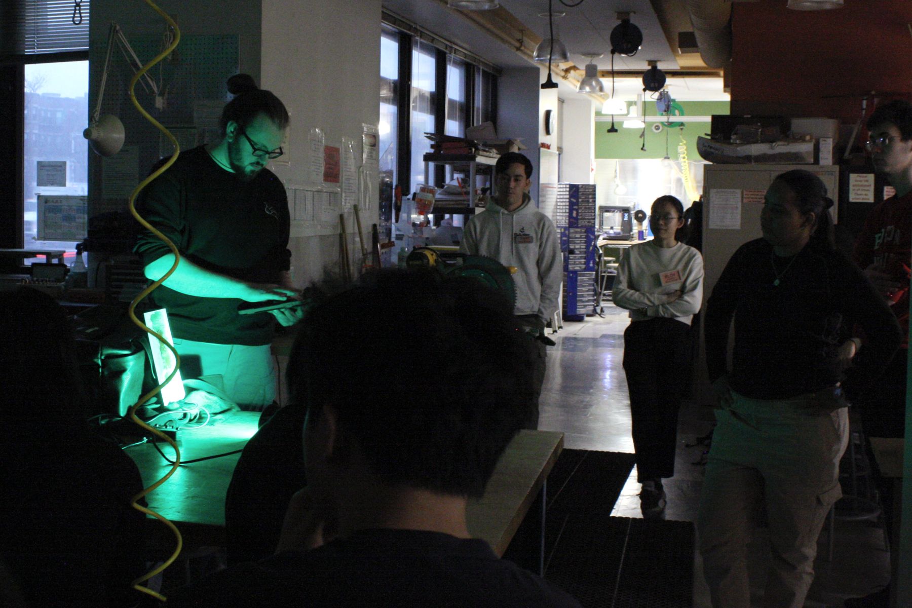 Students clustered closer together in a dark room to watch a lighting color demo