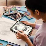 Back view of woman artist drawing on digital tablet while sitting in living room