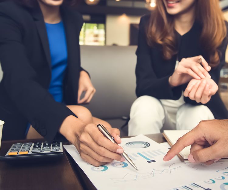 A group of three business individuals at a table, engaged in discussion with papers and a calculator in front of them.