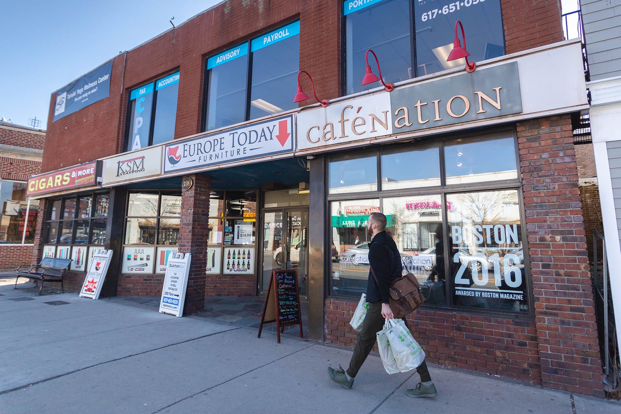 Photo of the outside of Cafe Nation; person with shopping bags walks down the block.