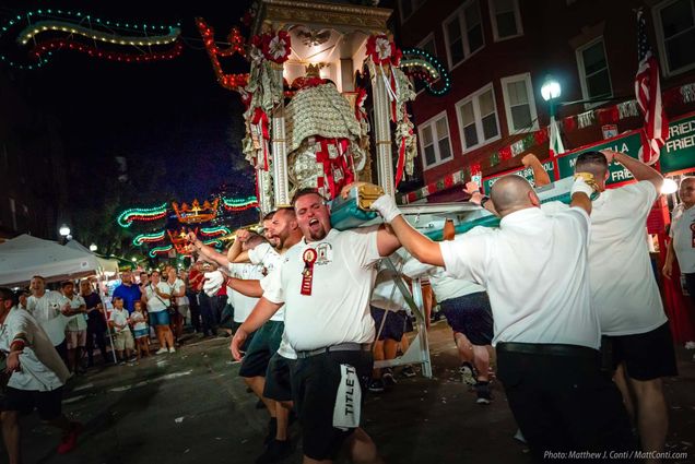 Photo of the St. Agrippina’s Feast celebration. A group of men hoist an ornate statue as the parade and shout during the night in the North End street.