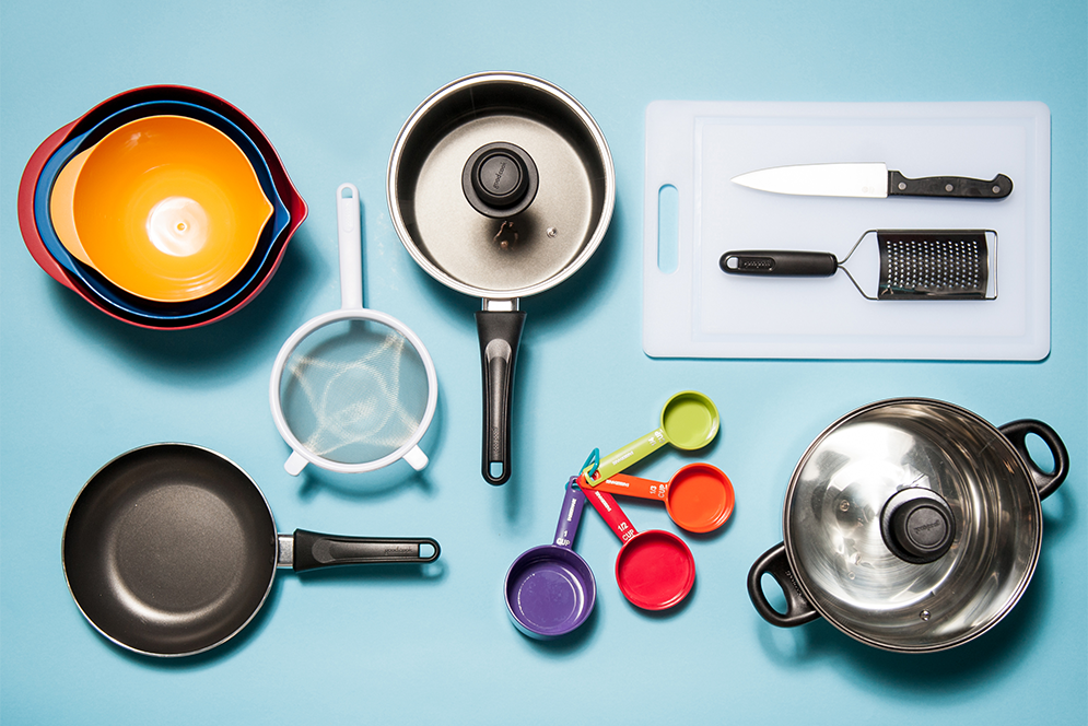 Set of basic kitchen utensils including mixing bowls, sauce pan, non-stick pan, stockpot, strainer, cutting board, chef's knife, grater, and measuring cups