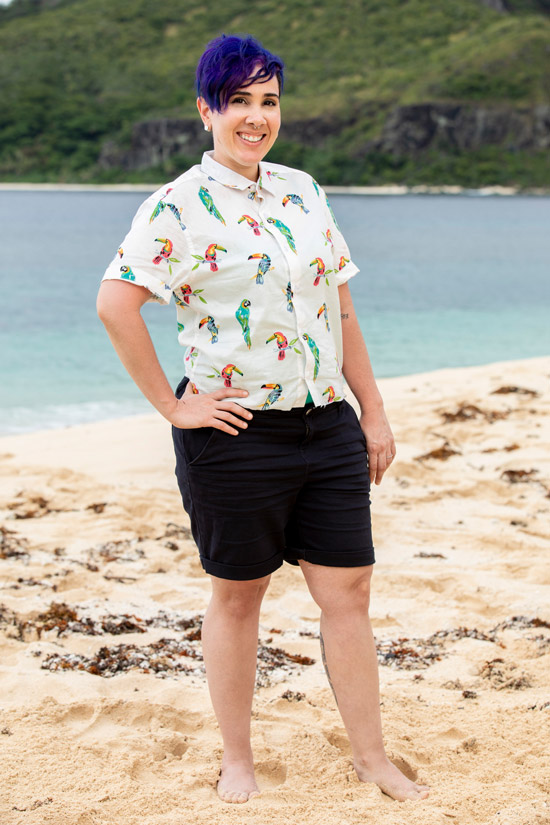 幸存者 contestant Lyrsa 托雷斯 and BU alum poses on a white sandy beach in a button down shirt with colorful Toucans