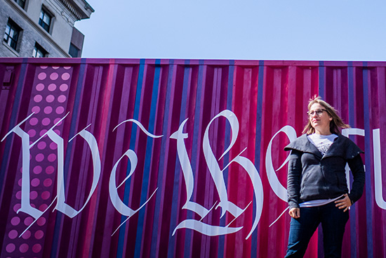 Director of Art and Creative Initiatives, HUBWeek, poses for a photo in front of a recycled shipping container transformed into a piece of artwork with the slogan 'We the Future'