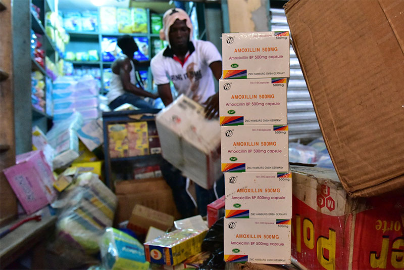 Behind a stack of cartons of fake Amoxicillin BP, a Health Ministry employee takes part in an operation to empty shops selling fake medicine during a raid monitored by police officers against shops selling counterfeit drugs on May 3, 2017 at the Adjame market in Abidjan.