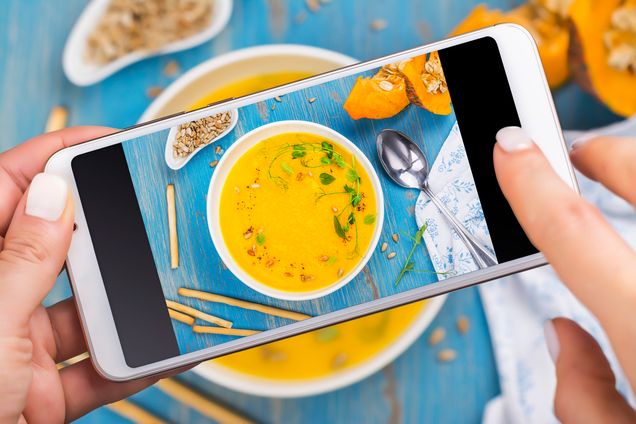 Woman taking photo of fall spicy pumpkin soup with herbs, croutons and sunflower seeds. Trendy instagram photo shot. Top view, flat lay style. Copy space
