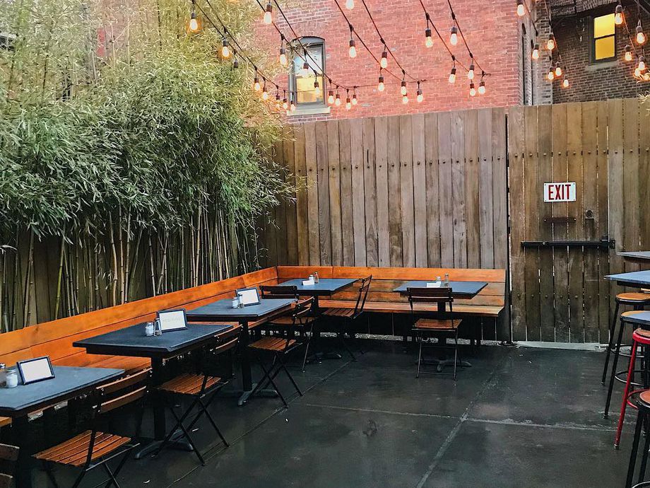 Photo of Audubon’s patio, which has a dark gray floor and is fenced in with a tall wooden fence. Bamboo plants run along the left behind bench seating.