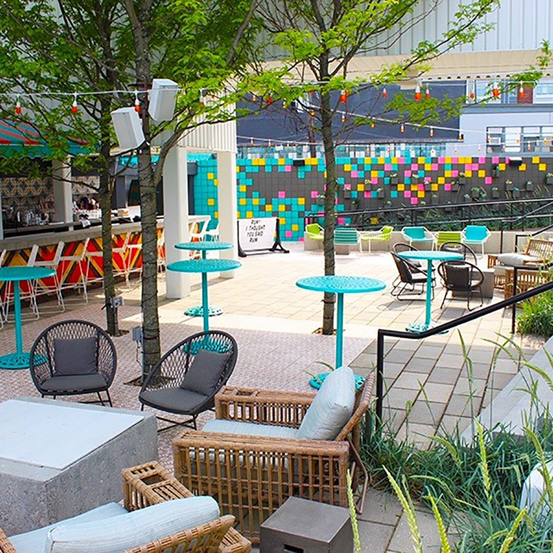 Photo of patio of Casa Cana, which has outdoor tile floor, brightly colored tables, a few wicker seats, and colorful mural along the back wall.
