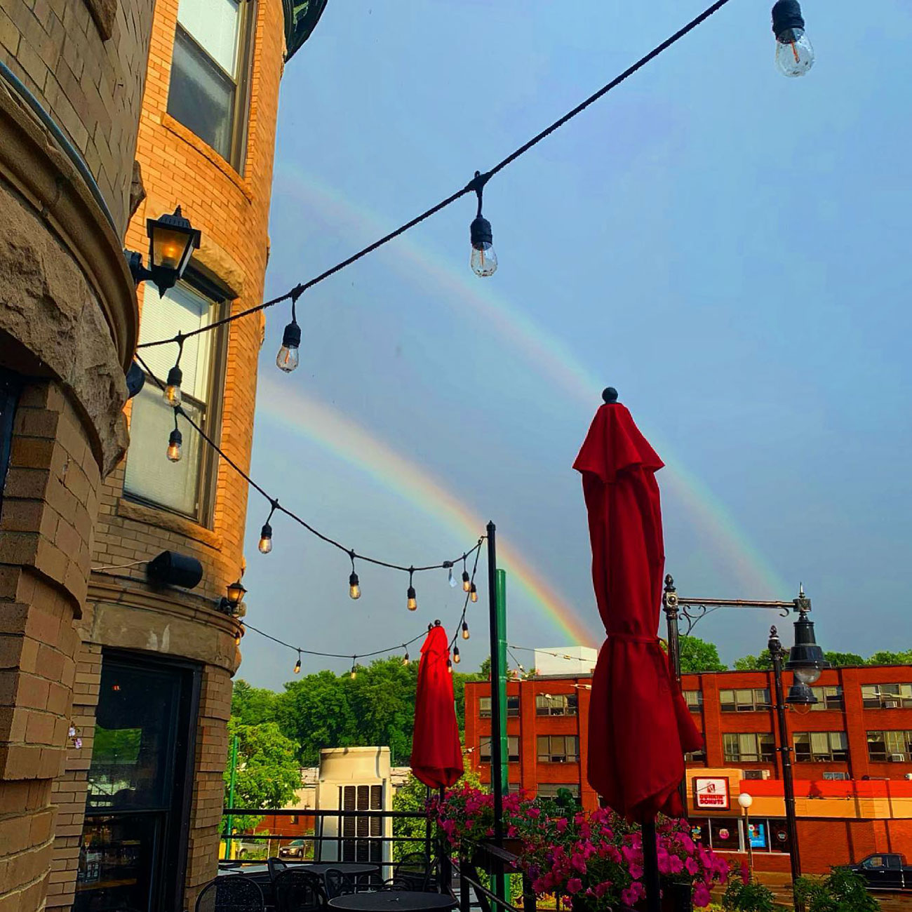 Photo of a rainbow over the tables outside Cityside Tavern. The umbrellas are red and tied up.