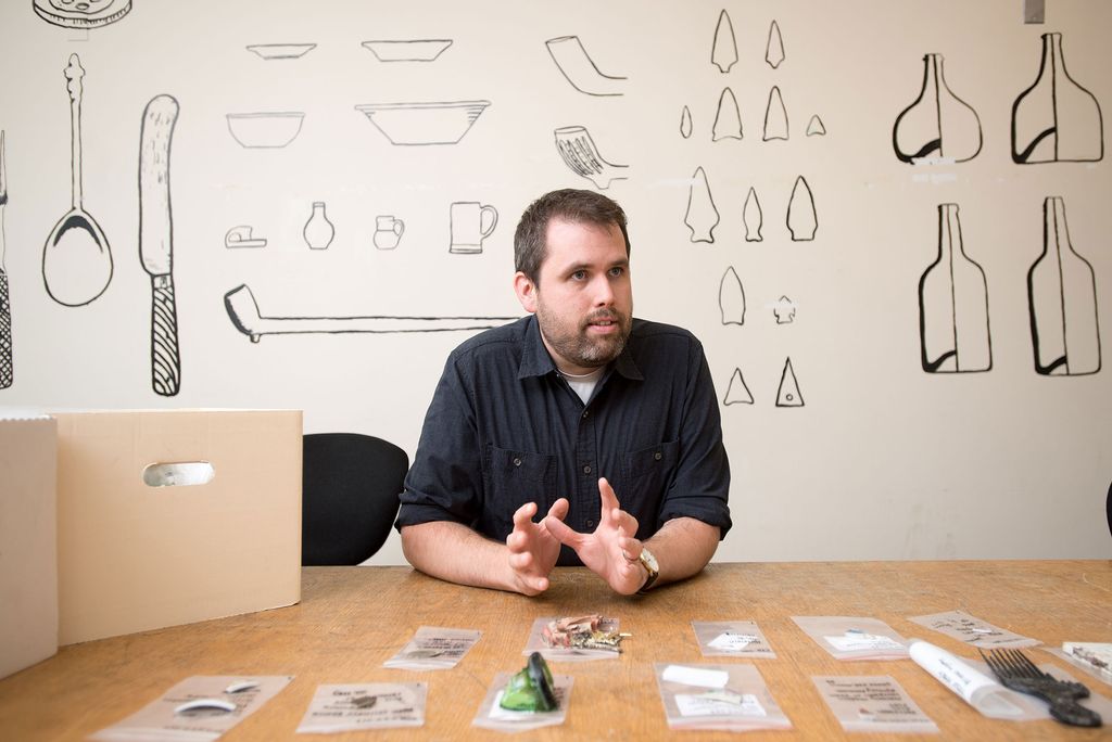 Joe Bagley discusses his archaeological dig in Boston's Chinatown neighborhood with artifacts found in the dig laid out on the table in front of him.