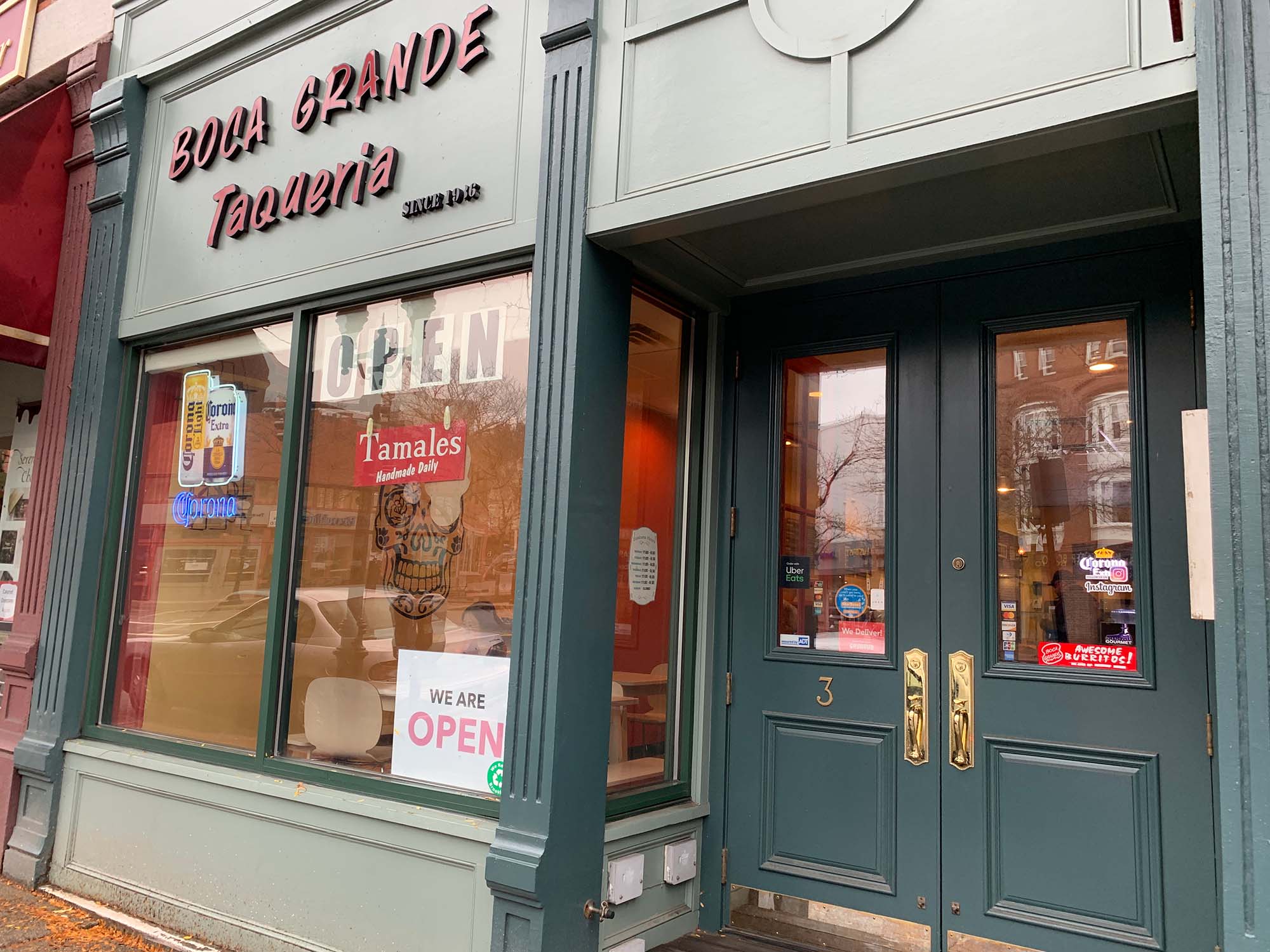Photo of the exterior of Boca Grande Taqueria. A sign in the window says "Open," another reads "tamales"