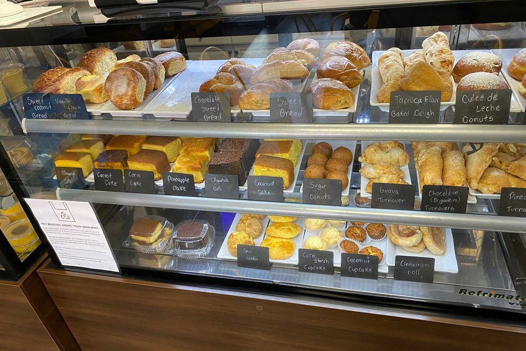 Photo of a pastry case at Cafe Brazil Bakery. Some of the desserts seen include: sweet coconut bread, chocolate sweet bread, coconut cake, pineapple cake, corn starch cupcake, guava turnover, and many more.