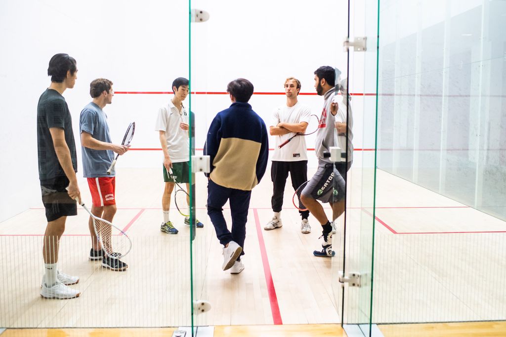 The BU club squash team chats on a court before a practice