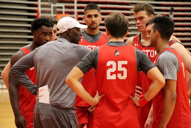 Men's basketball team huddles up around their coach during practice