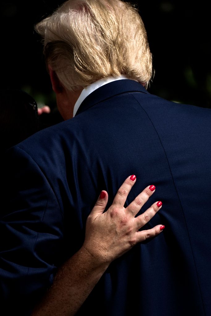 A woman's hand with red-painted finger nails is placed on Trump's back