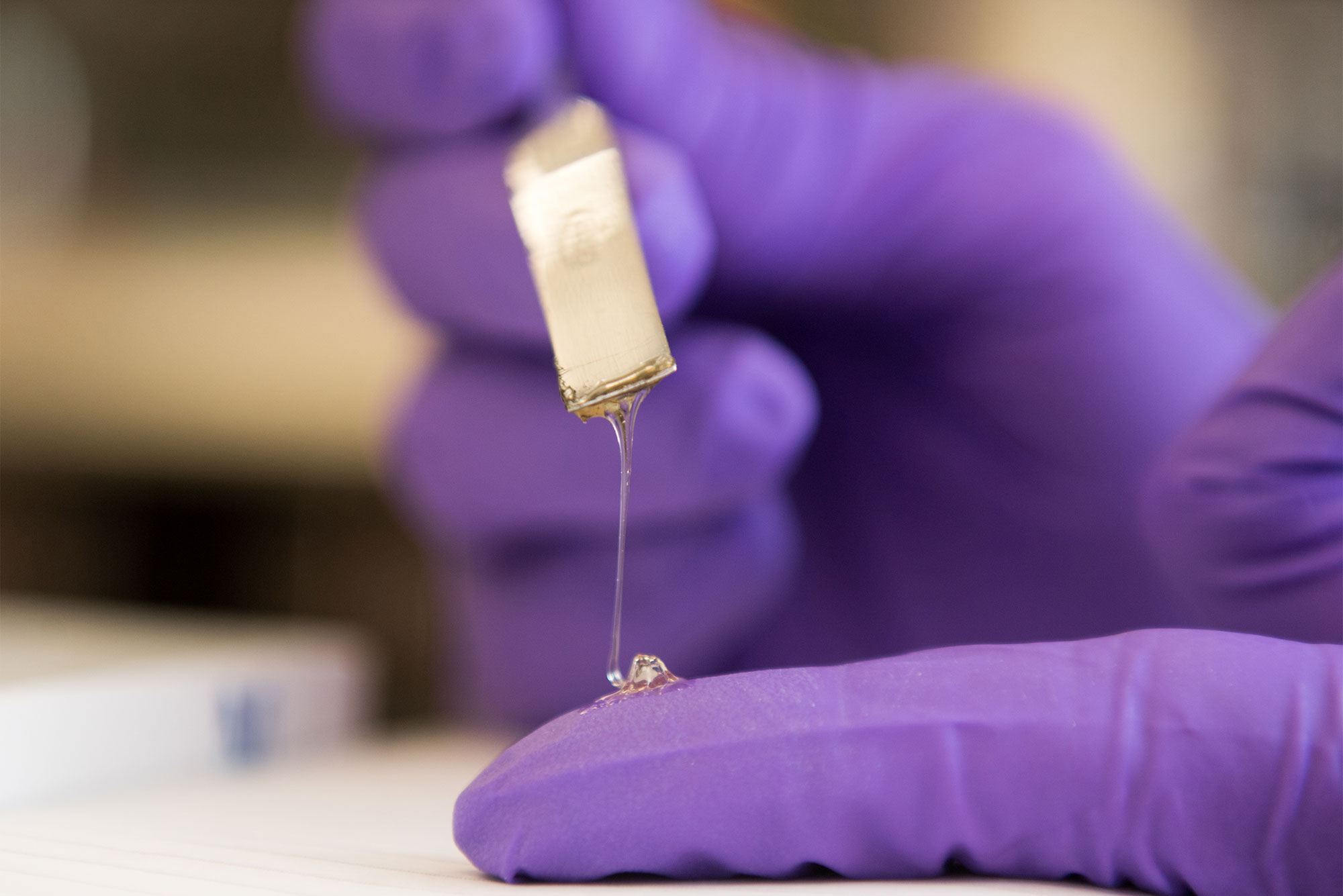 Detail photo of a clear sustainable adhesive substance dripping onto a fingewr
