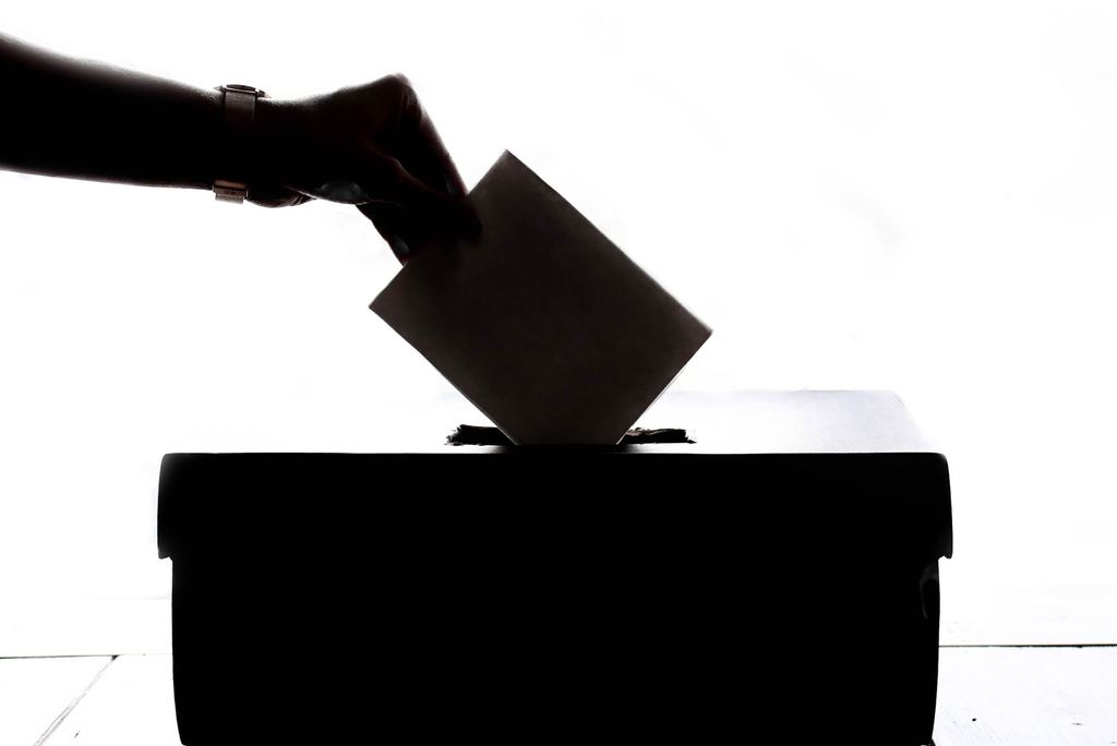 A silhouette photo of a person's arm casting a ballot into a ballot box.