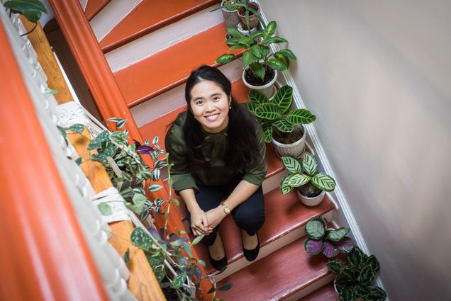 Minh-Thuy Nguyen sits on orange stairs lined with all of her plant babies