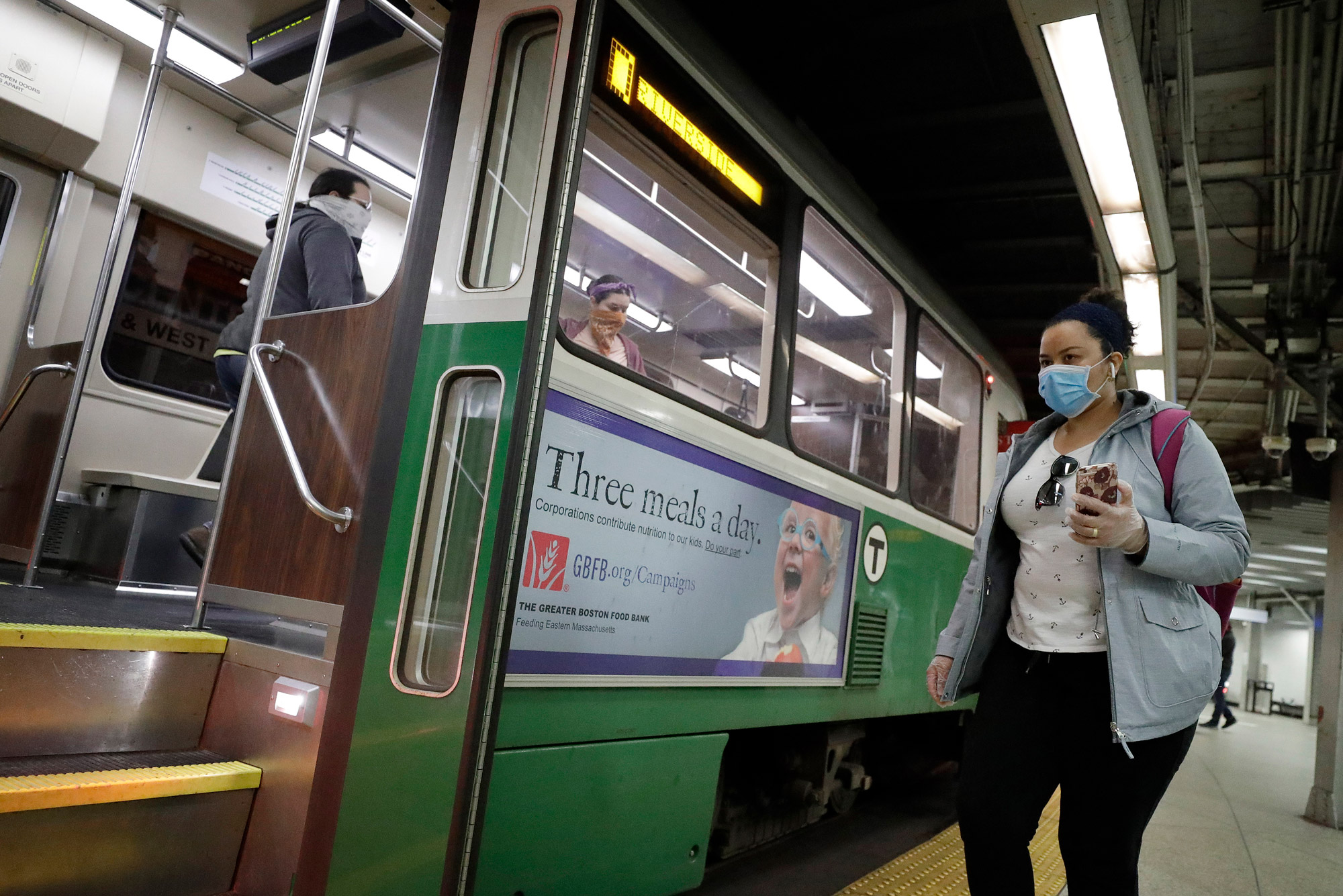 A photo of a woman in a mask holding her phone while she boards and MBTA green line train
