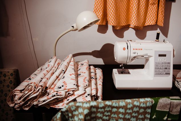 A folded pile of cloth with Rhett and the words "Boston University" on it sits next to a sewing machine and light.