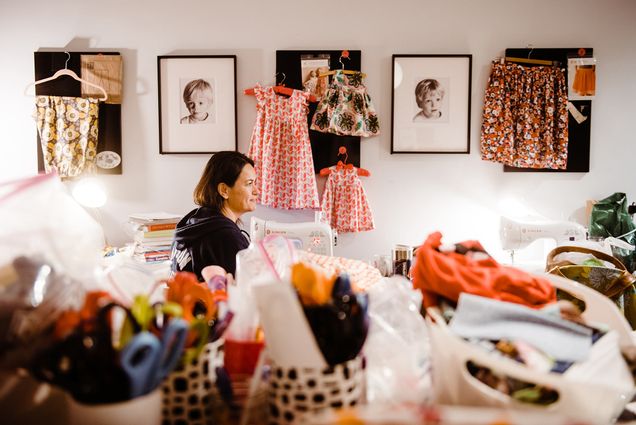 Image of Annissa Essaibi-George, sitting in her business, Stitch House, in Dorchester. Annissa is helping to sew face masks for the Boston University Police Department. A table of crafting supplies is seen in the foreground.