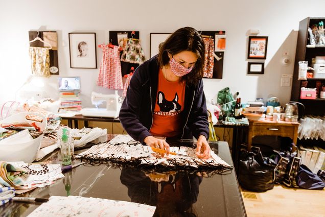 Image of Annissa Essaibi-George, cutting fabric. Annissa is helping to sew face masks for the Boston University Police Department at the Stitch House in Dorchester. A sewing machine is o behind her.