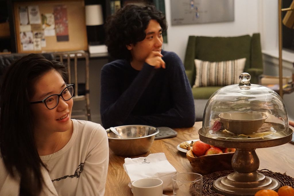 Photo taken during an open hours session at Kinh Vu’s apartment. Two students look down across the table, where snacks are laid out.
