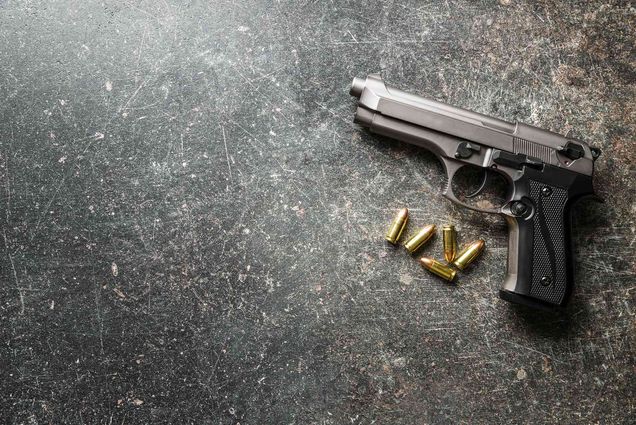 Image of a handgun with gold bullets on a scratched rock surface.