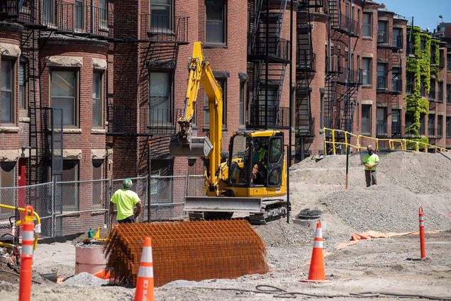 Photo of limited construction continuing at the Center for Data and Computer Sciences on Granby Street May 20. A yellow excavator with its basket raised. Two construction workers standby. Orange traffic cones are seen in the foreground.