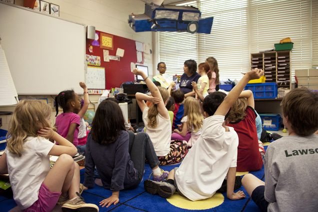 Photo of a daycare classroom where some students raise their hands.