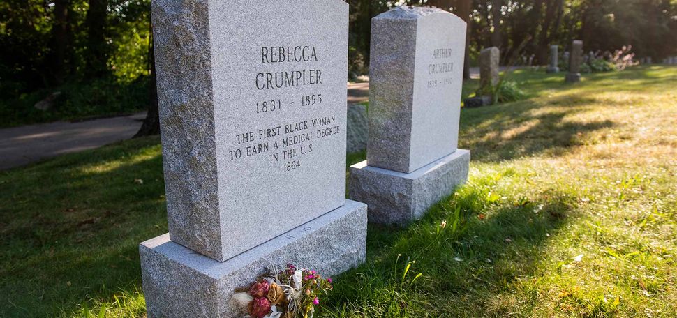 Photo of the headstones of Rebecca Lee Crumpler (MED'1864), reading "the first Black woman to earn a medical degree in the US." and her husband Arthuer Crumpler. The headstones are at the Fairview Cemetery in Hyde Park. Bright green grass grows around the headstones.