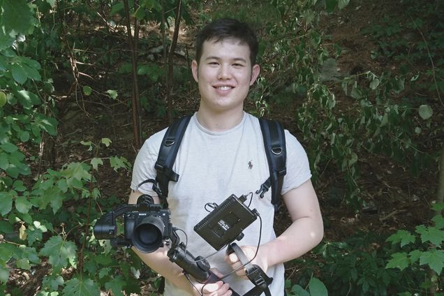 Photo of junior neuroscience major Shota Weaver (CAS’22) has been capturing footage of New England’s wildlife and creating short films. Here he holds camera gear and wears a backpack while standing in the woods.