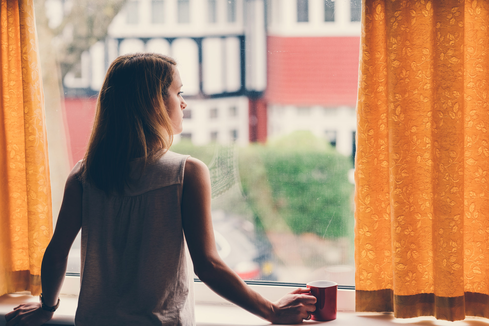 A photo of a woman holding a coffee mug staring out of a window
