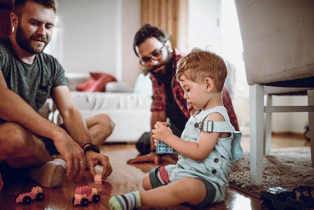 A photo of two dads sitting playing with their child