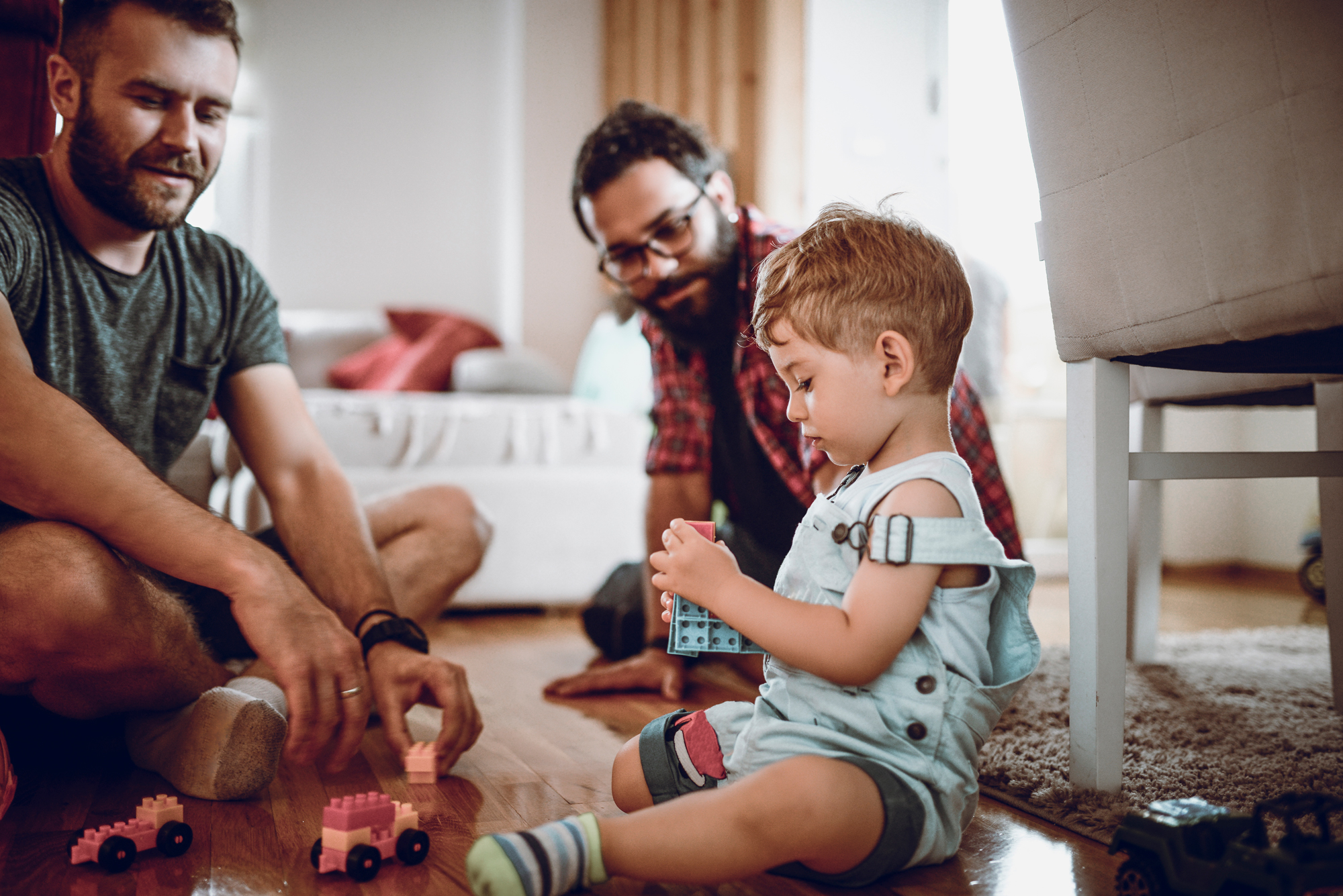 A photo of two dads sitting playing with their child