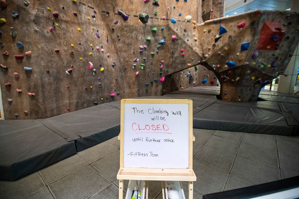 Photo of the rock climbing wall in FitRec. The wall is empty and a white board sign in front of the wall reads "the climbing wall will be closed until further notice. -FitRec team"