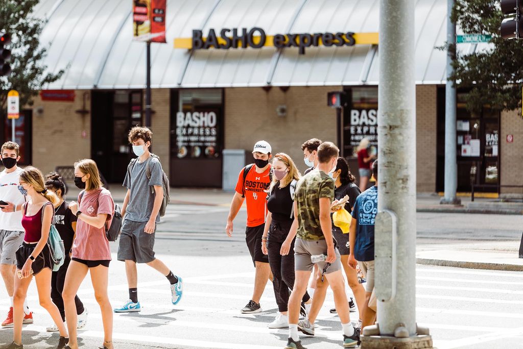 Photo of students crossing Comm Ave near Marsh plaza during move-in 2020. All of the students wear masks and wear summer clothing.