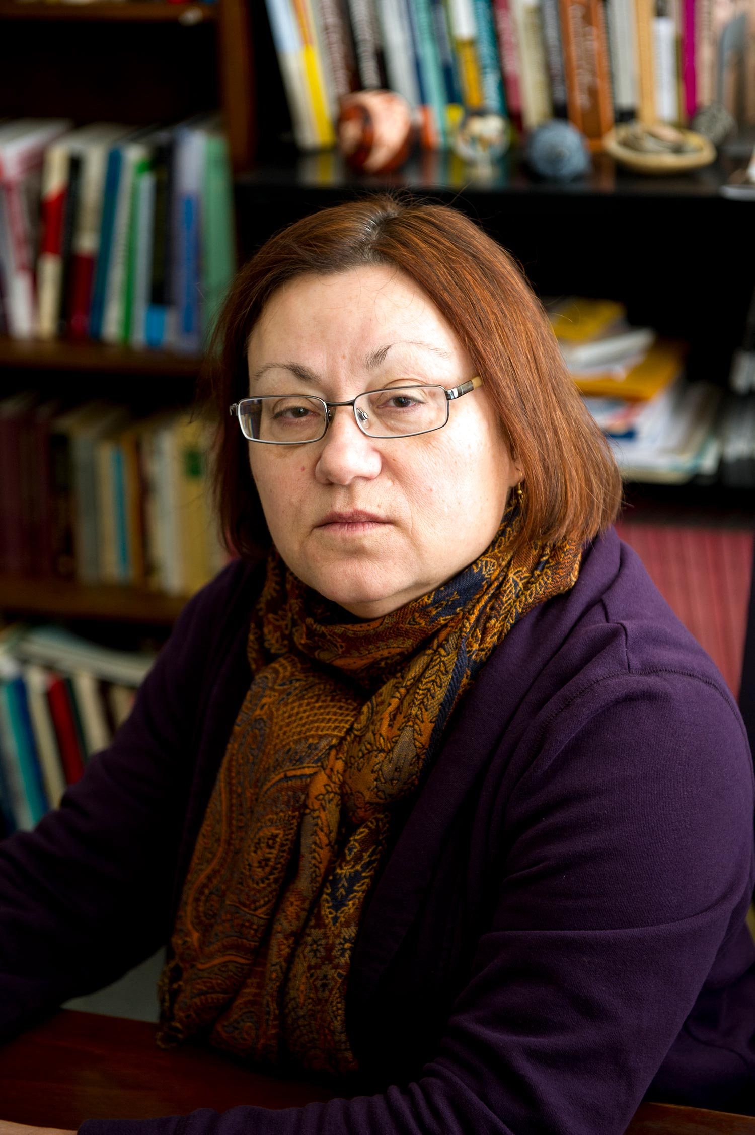 Portrait of professor Mary Beaudry, who died unexpectedly on October 20. She wears a orange colored scarf and purple sweater in her study.