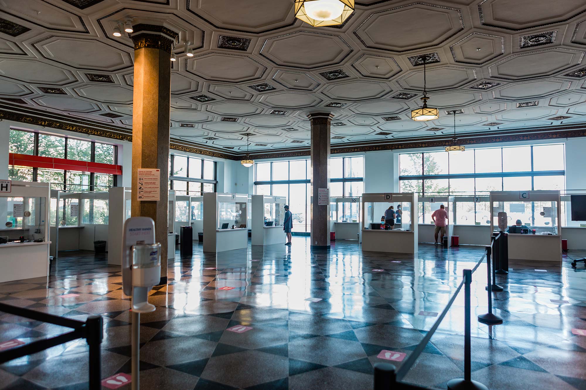 Photo of a Covid-19 collection site at 808 Commonwealth Ave. The floor is divided by black dividers and white booths where people get tests are seen in the background.