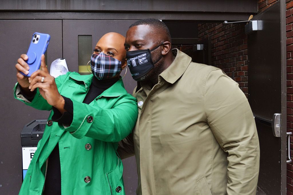 Photo of Representative Ayanna Pressley (D-Mass. 7th) taking a selfie with her husband after voting on October 24, 2020. Pressley wears a bright green jacket and her husband's mask reads "vote," Both look happily at Pressley's phone as she takes a selfie.