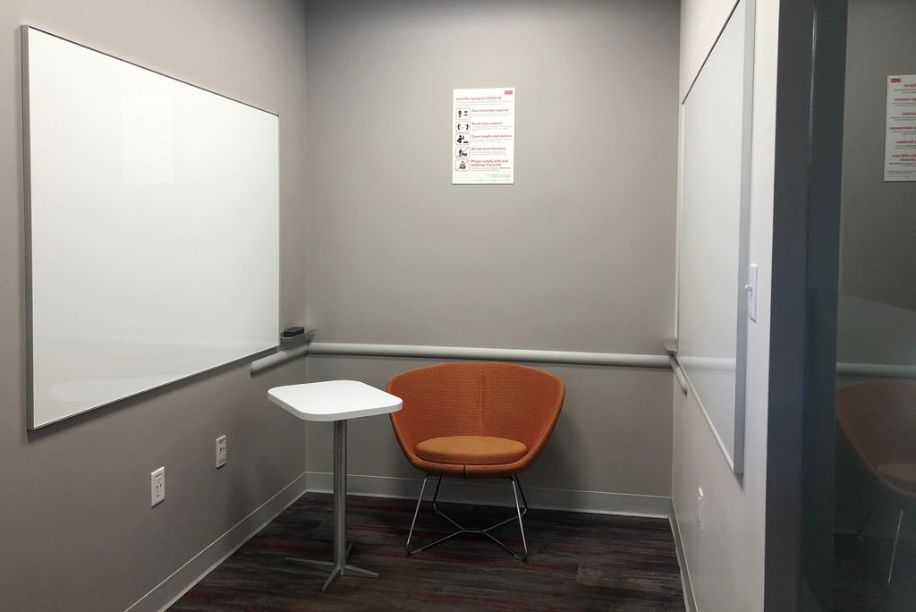 Photo of a small reservable room with a side table and orange seat. A whiteboard hangs on the wall.