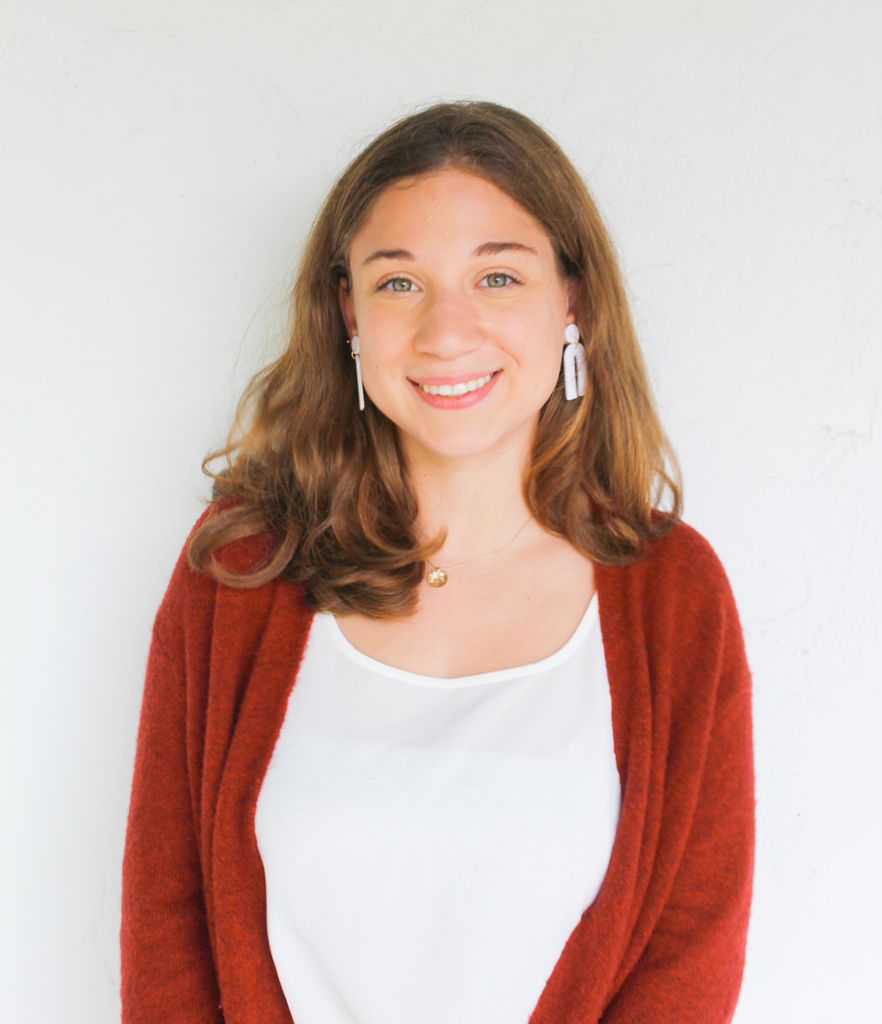 Headshot of Emily Lynn Perelman who smiles and wears a red cardigan.