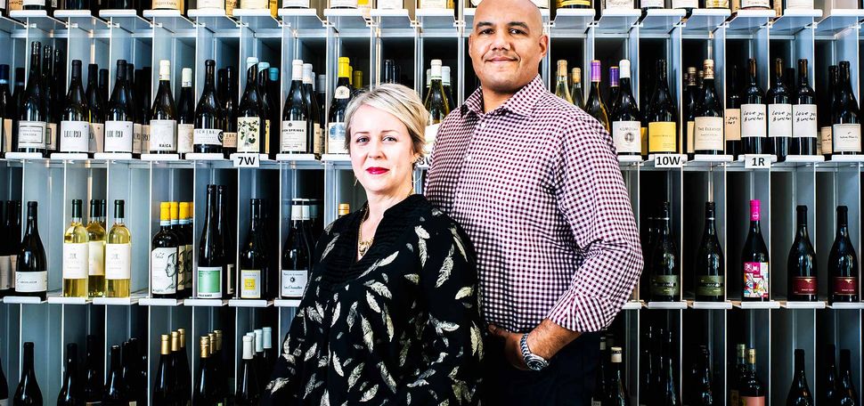 TJ and Hadley Douglas, owners of Urban Grape in Boston, pose for a photo on November 2, 2020. A floor to ceiling rack of wine bottles is seen behind them.
