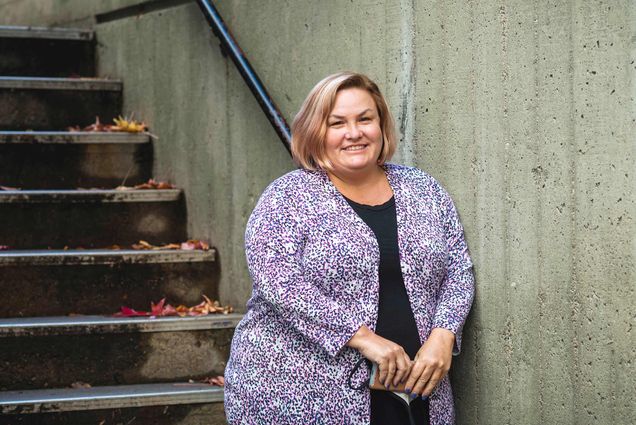 Photo of Amy Goodrich, director of catering at BU, in a colorful sweater posing at the bottom of a staircase.