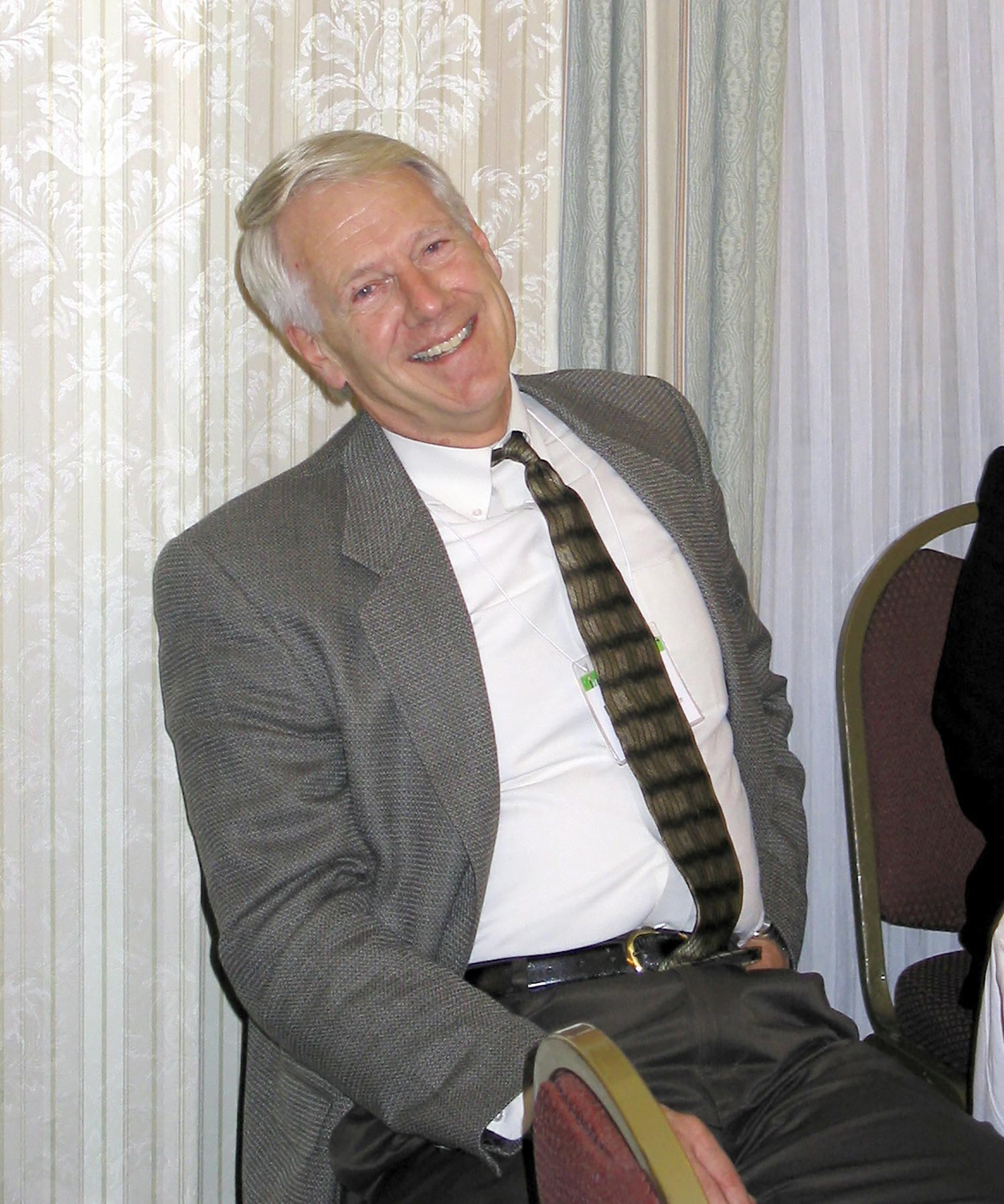 Photo of William A. Anthony sitting in a chair in a suit and tie and smiling.