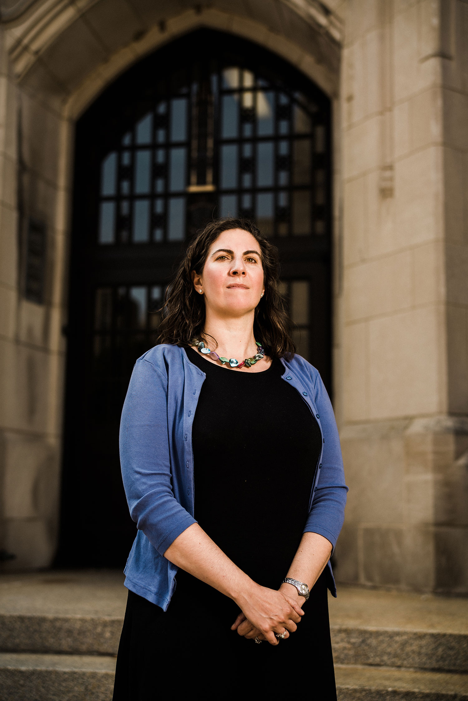 Portrait of Wheelock College Associate Professor, Kathleen Corriveau, standing outside what looks like the entrance to a church in shale blue sweater and black dress.