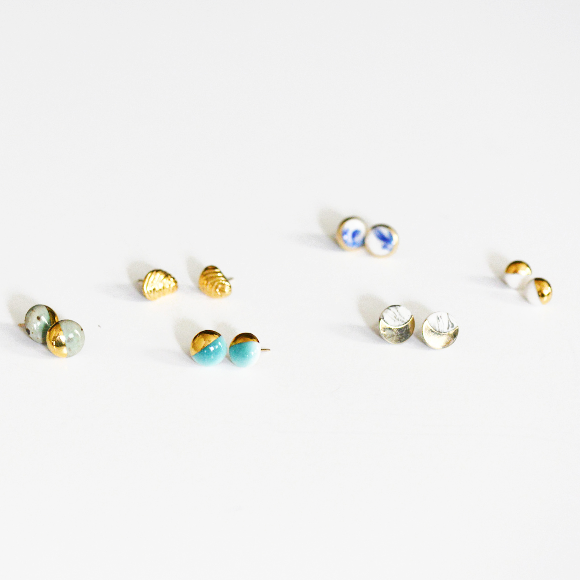 Photo of six pairs of part-gold, part-porcelain earrings sitting on a white surface.