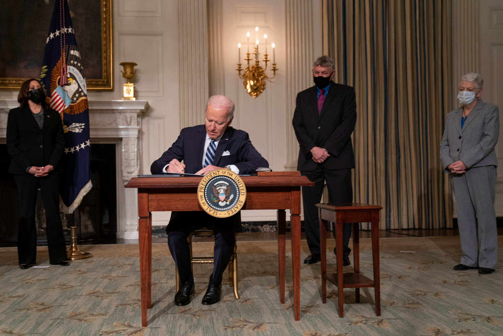 A photo of Joe Biden signing climate legislation at a desk in front of Vice President Kamala Harris and another administration officials