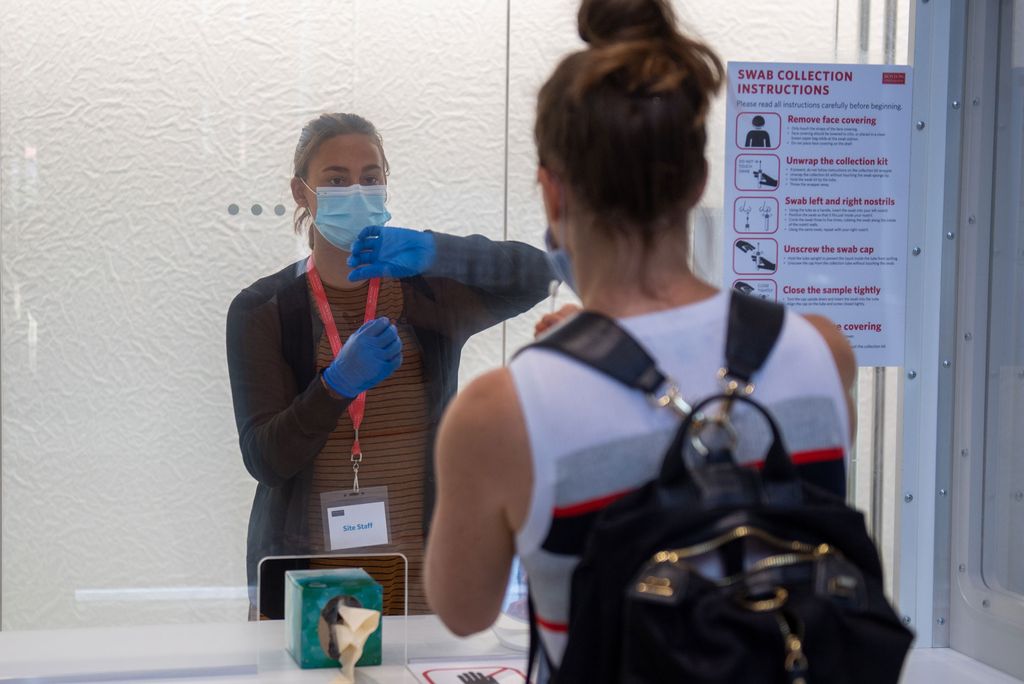 A photo of a COVID-19 testing station at BU. A worker instructs a student how to swab their nose.