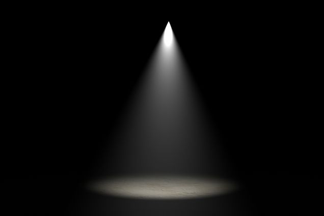 Photo of stage light shining directly down onto a stage in a completely dark room.